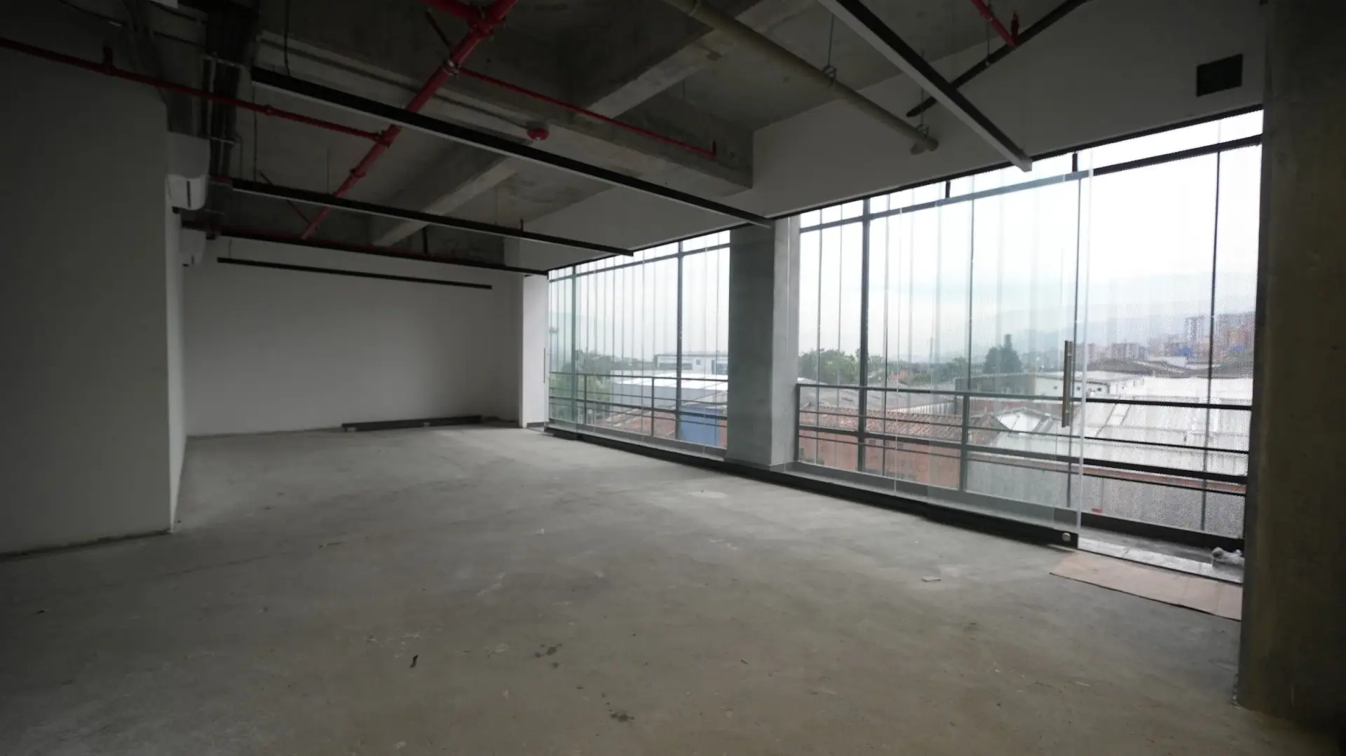 Oficina vacía en obra gris de Ayurá Center, con ventanales de piso a techo y vista a la ciudad