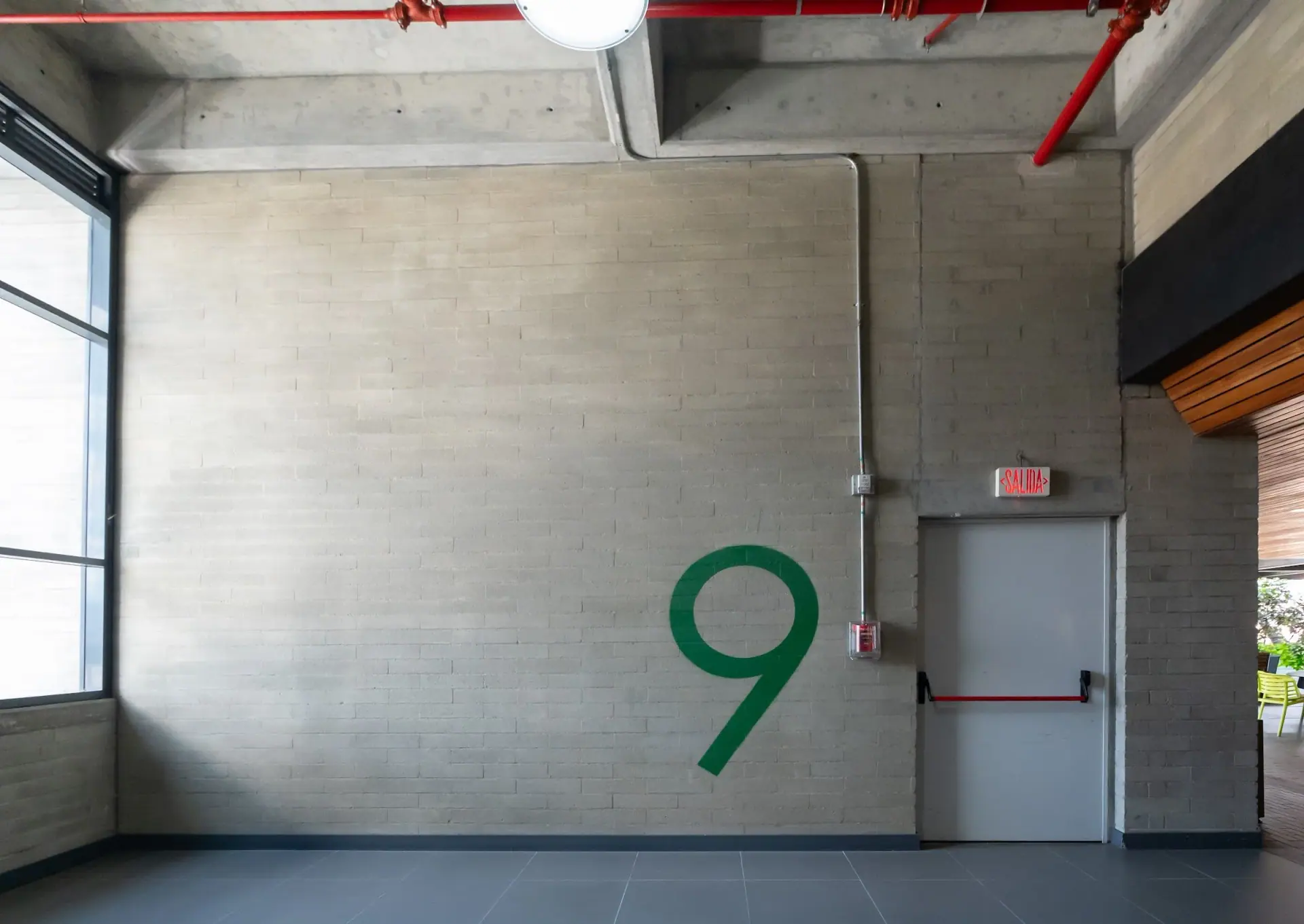 Hall del piso 9 de Ayurá Center con muro de concreto, el número 9 pintado en verde y una ventana lateral
