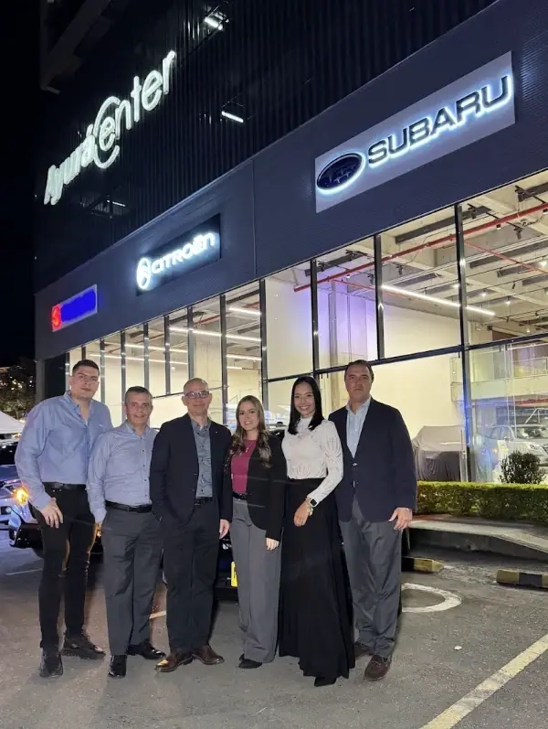 Seis personas del equipo de la alianza con Inchcape posan de noche frente a las vitrinas de Suzuki, Citroën y Subaru en Ayurá Center