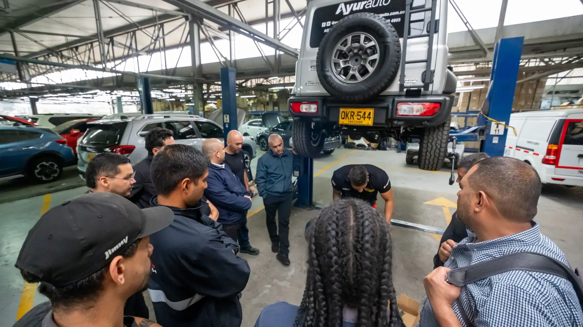Técnicos de Ayurauto en una capacitación en el taller, reunidos alrededor de un Suzuki Jimny levantado en el elevador