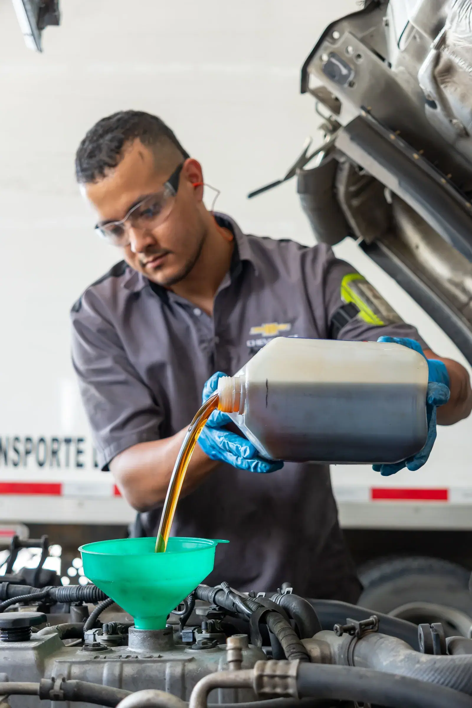 Técnico del taller diésel vierte aceite en el motor de un camión con un embudo verde